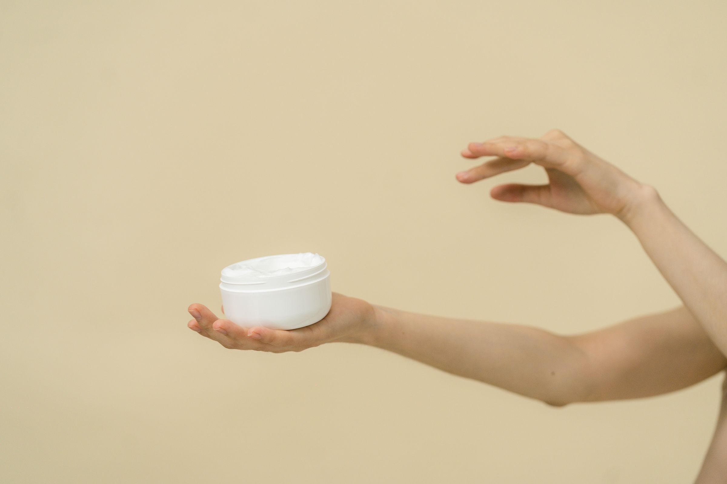 白いクリーム容器を手に持つスキンケアのイメージ